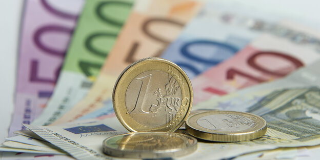 Eine gläneznde Ein-Euro-Münze steht auf Geldscheinen aus Papier Eine gläneznde Ein-Euro-Münze steht auf Geldscheinen aus Papier