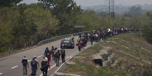 Migranten aus Mittelamerika gehen mit Rucksäcken auf dem Rückeneine Straße entlang Migranten aus Mittelamerika gehen mit Rucksäcken auf dem Rückeneine Straße entlang