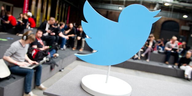 Ein Aufsteller des Twitter-Vogels steht in einem Raum. Drumherum sitzen MEnschen, die an Rechnern arbeiten Ein Aufsteller des Twitter-Vogels steht in einem Raum. Drumherum sitzen MEnschen, die an Rechnern arbeiten