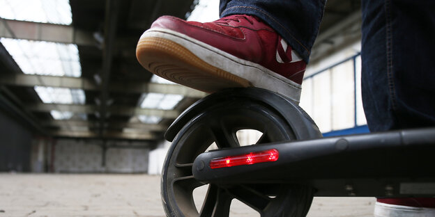 Auf dem Rad eines E-Scooters setzt eine Person ihren Fuß ab Auf dem Rad eines E-Scooters setzt eine Person ihren Fuß ab