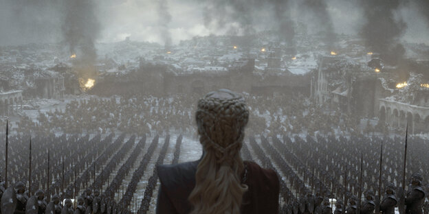 Game-of-Thrones-Szene: Frau von hinten, vor ihr Truppen in einer zerstörten Stadt Game-of-Thrones-Szene: Frau von hinten, vor ihr Truppen in einer zerstörten Stadt