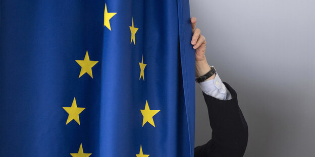 Eine Person zieht einen Vorhang zu, auf den eine Europafahne gedruckt ist Eine Person zieht einen Vorhang zu, auf den eine Europafahne gedruckt ist