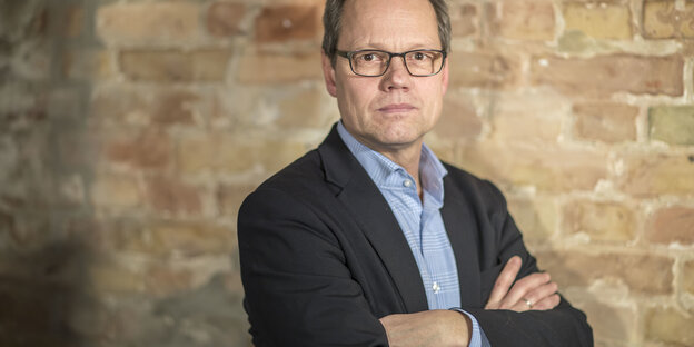 Mann mit verschränkten Armen, im Anzug, vor Backsteinwand Mann mit verschränkten Armen, im Anzug, vor Backsteinwand