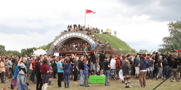 Ein grasüberwachsener Hangar - drumherum viele Leute, die feiern Ein grasüberwachsener Hangar - drumherum viele Leute, die feiern