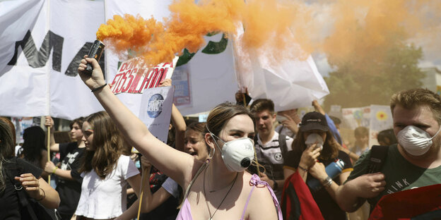 Eine Demonstrantin hält eine orangene Rauchfackel in der Hand, während Schülerinnen und Schüler mit Protestplakaten und Bannern während des Fridays for Future Eine Demonstrantin hält eine orangene Rauchfackel in der Hand, während Schülerinnen und Schüler mit Protestplakaten und Bannern während des Fridays for Future