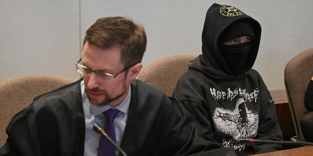 Eine vermummte Frau sitzt neben einem Mann im Anzug Eine vermummte Frau sitzt neben einem Mann im Anzug