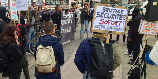 DemonstrantInnen mit Schildern stehen um eine Verstärkeranlage.