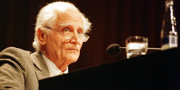 Michel Serres steht weißhaarig an einem Pult, vor ihm ein Mikro und ein Glas Wasser Michel Serres steht weißhaarig an einem Pult, vor ihm ein Mikro und ein Glas Wasser