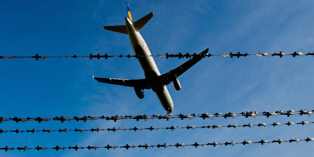 Flugzeug am Himmel, davor ist Stacheldraht zu sehen Flugzeug am Himmel, davor ist Stacheldraht zu sehen