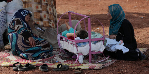 Zwei Frauen und ein kleines Kind unter freiem Himmel in einem Flüchtlingscamp Zwei Frauen und ein kleines Kind unter freiem Himmel in einem Flüchtlingscamp