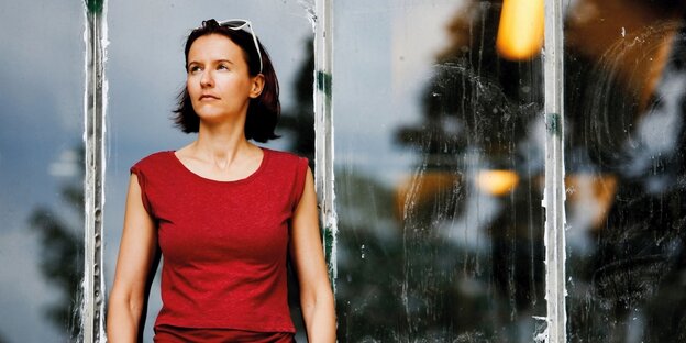 Eine Frau in einem roten T-Shirt lehnt sich an eine Glaswand Eine Frau in einem roten T-Shirt lehnt sich an eine Glaswand