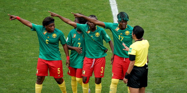 Vier Fußballerinnen stehen nebeneinander und reden auf eine Schiedsrichterin ein, drei von ihnen zeigen mit ausgestecktem Arm mach rechtsoben