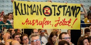 Besucher halten während der Rede von Kanzlerin Merkel Anfang Juni bei der Jahreskonferenz des Rates für Nachhaltige Entwicklung ein Transparent mit der Aufschrift "Klimanotstand Ausrufen, jetzt!"