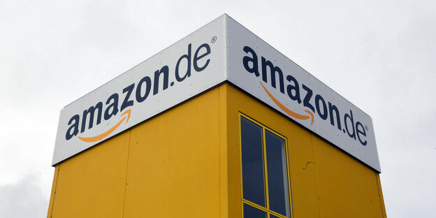 Man sieht ein amazon.de-Logo auf zwei Seiten eines Logistikgebäudes.