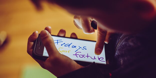 Eine Hand tippt auf einem Smartphone. Auf dessen Bildschirm steht „Fridays for future“