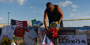 Ein Mann beugt sich über Blumen und Schildern mit Beileidsbekundungen und US-Flaggen in El Paso