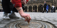 Eine Hand wirft eine Münze in einen Gulli vor dem Bremer Rathaus, der als Spendenbox dient