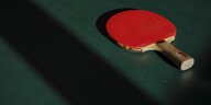 Eine rote Tischtennis-Kelle liegt auf einer grünen Tischtennis-Plattte