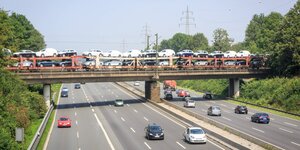 Ein mit etlichen PKW beladener Autozug überquert auf einer Eisenbahnbrücke die Bundesstraße B1. Darunter fahren vereinzelte Autos in beide Verkehrsrichtungen