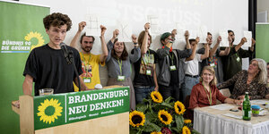 obert Funke (l, Bündnis 90/Die Grünen), Sprecher der Grünen Jugend Brandenburg, spricht auf dem kleinen Parteitag der Grünen in Brandenburg, während andere Mitglieder der Grünen Jugend Schilder mit Buchstaben hochhalten, die die Aufschrift "#Keenja" ergeb
