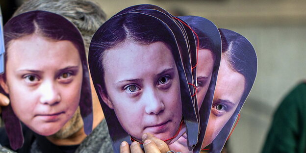 ein Mann hält sich mehrere Greta-Thunberg-Masken vors Gesicht