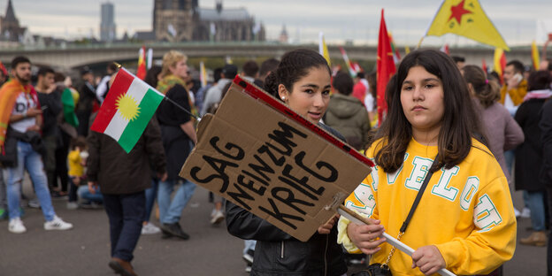Eine Frau steht mit einem Schild auf einer Demo, darauf steht „Sag nein zum Krieg“