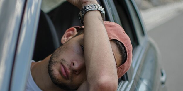 Ein junger Mann sitzt im Auto und bedeckt sein Gesicht mit seinem Arm