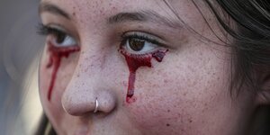 Gesicht einer jungen Frau, die sich Tränen aus Blut unter die Augen geschminkt hat