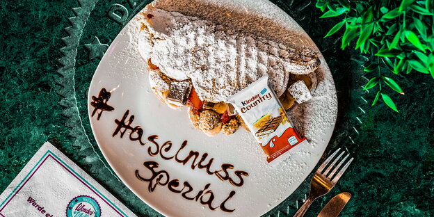 Eine reich verzierte Waffel auf einem Teller, auf dem #Haselnuss Spezial in Schokosauce geschrieben steht