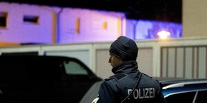 Ein Polizist steht in Hanau vor einem Haus, das in blauem Licht leuchtet.