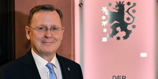 Bodo Ramelow vor rosa Hintergrund mit Thüringer Staatswappen