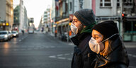 Zwei junge Leute mit Masken wegen Corona-Virus überqueren die Kreuzung am Checkpoint Charlie in Berlin.