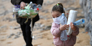 Mädchen sammel Plastikflaschen am Strand auf