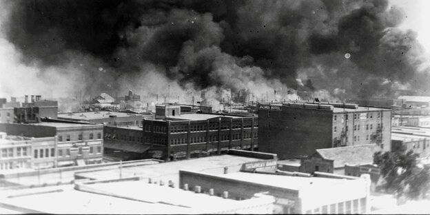 Ein Schwarz-weiß-Foto - Ansicht einer Stadt von erhöhter Perspektive. Dichter schwarzer Rauch steigt über den Dächern auf