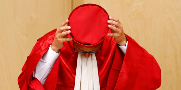 Andreas Vosskuhle, Präsident des deutschen Bundesverfassungsgerichts, setzt seinen roten Hut wieder auf.