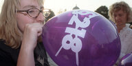 eine Frau bläßt einen lila Luftballon auf, darauf steht durchgestrichen "§218"