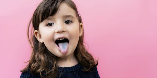 Kind vor pinkem Hintergrund streckt die Zunge heraus.