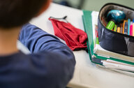 Eine Mund-Nasen-Bedeckung liegt während einer Unterrichtsstunde einer fünften Klasse des Friedrich-Schiller Gymnasiums neben einem Mäppchen und Schulbüchern auf einem Schultisch.