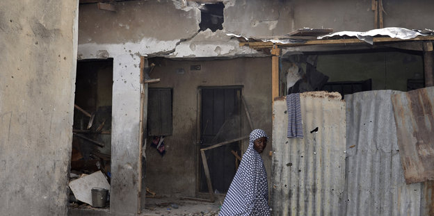 Eine Frau geht an einem beschädigten Haus vorbei