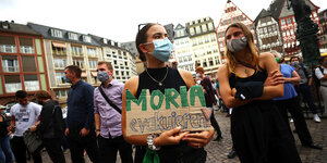 Eine Frau steht auf einem Platz in Frankfurt in einer Menschenmenge und hält ein Schild in den Händen auf dem steht: "Moria evakuieren"
