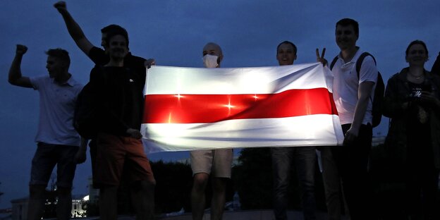 Люди держат флаг белорусской оппозиции, который светится в темноте