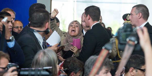 Eine Frau hebt den Arm und schreit umgeben von Journalisten und Sicherheitsleuten Eine Frau hebt den Arm und schreit umgeben von Journalisten und Sicherheitsleuten