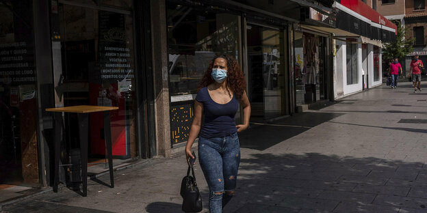 Eine Frau mit Mundschutzmaske ist allein auf einer Straße in Madrid unterwegs