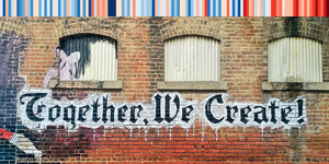 auf einer Backsteinhauswand steht der Spruch "Together we create"