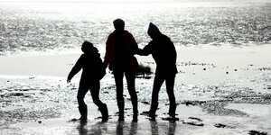 Zwei Erwachsene und ein Kind spazieren am Meer