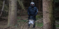 Ein Polizist mit Helm und in Uniform steht alleine zwischen Bäumen