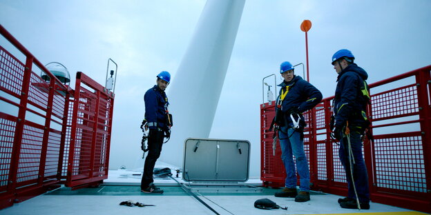 Drei Männer stehen auf der Plattform eines Offshore-Windparks. Drei Männer stehen auf der Plattform eines Offshore-Windparks.