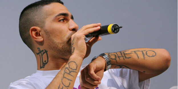 Der deutsche Rapper Bushido mit Mikrofon vor grauem Hintergrund. Der deutsche Rapper Bushido mit Mikrofon vor grauem Hintergrund.