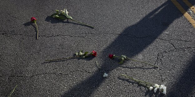 Einzelne Blumen liegen auf der Straße, der Schatten eines Menschen fällt darüber