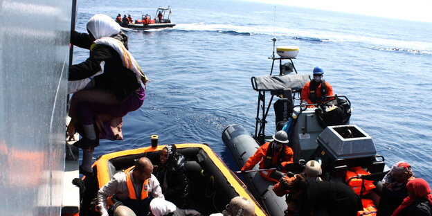 Eine Frau klettert aus einem Rettungsboot an Bord eines Schiffs. Eine Frau klettert aus einem Rettungsboot an Bord eines Schiffs.